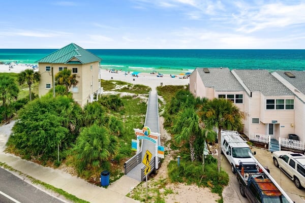 Beachfront resort pool with turquoise water, lounge chairs, umbrellas, and multi-story tan apartment buildings